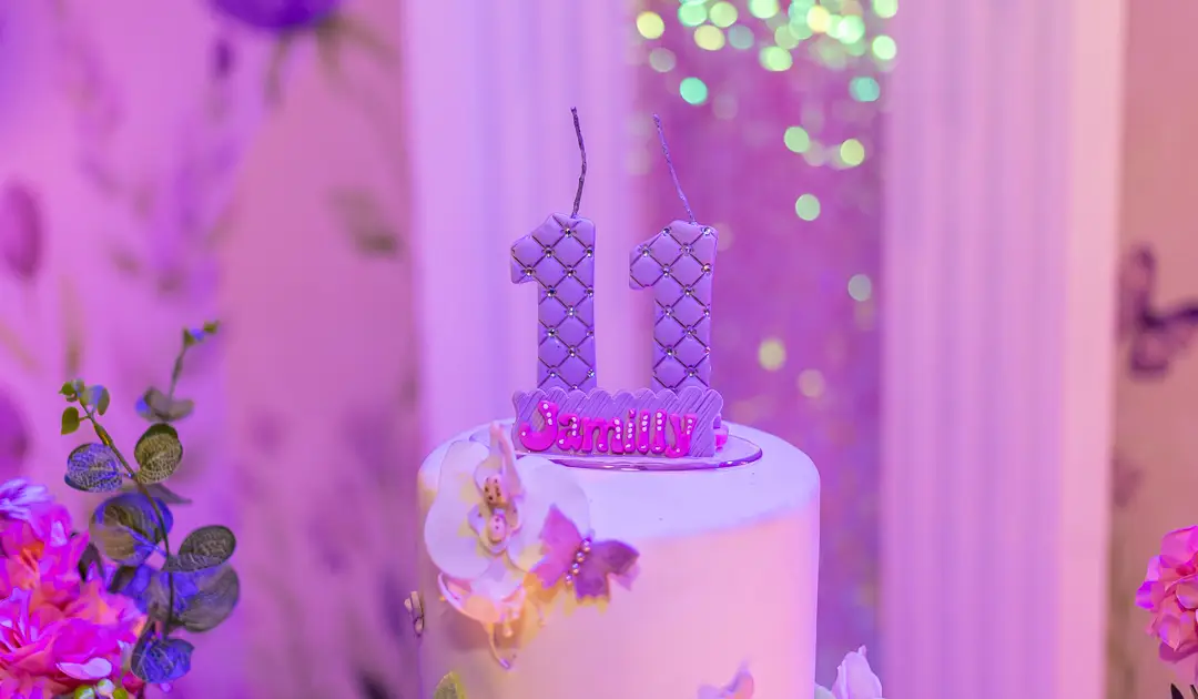 A imagem mostra um bolo de aniversário com velas lilás do número 11, representando uma das partes dos preparativos para uma festa de aniversário.