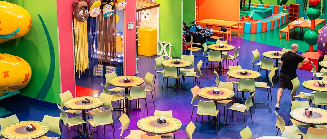 Salão da XVentura montado para a festa, com mesas infantis e a área de brinquedos ao fundo